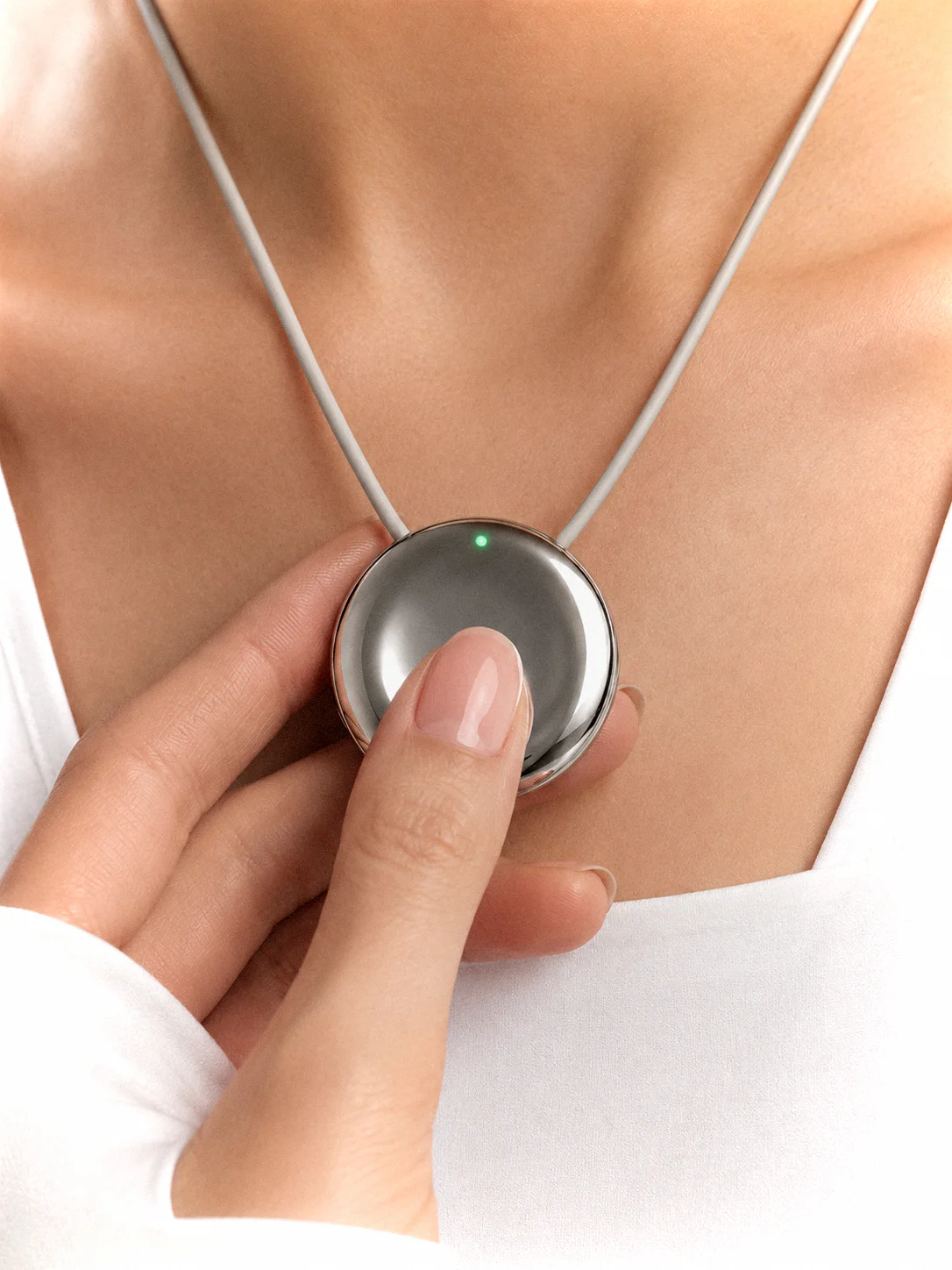 A thumb pressing the Pebb pendant worn on the chest