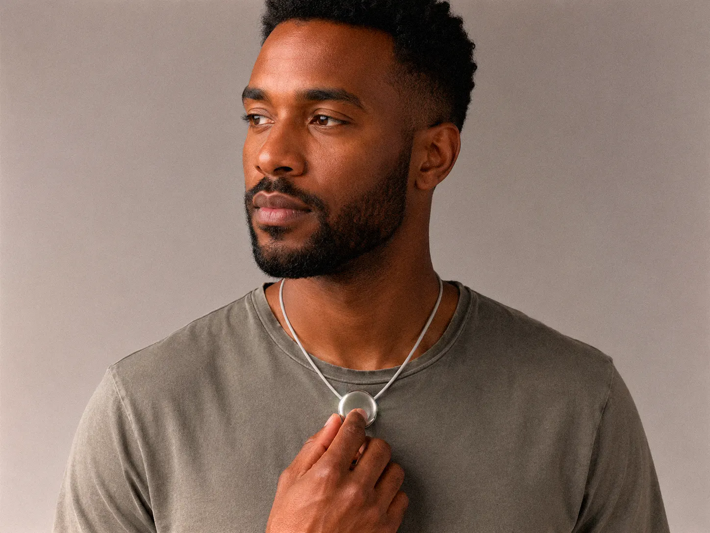 A man wearing Pebb on a cord, resting his hand on the pendant